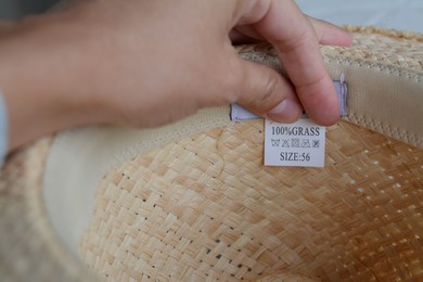 Photo of Woman holding white clothing label on straw hat, closeup. Space for text