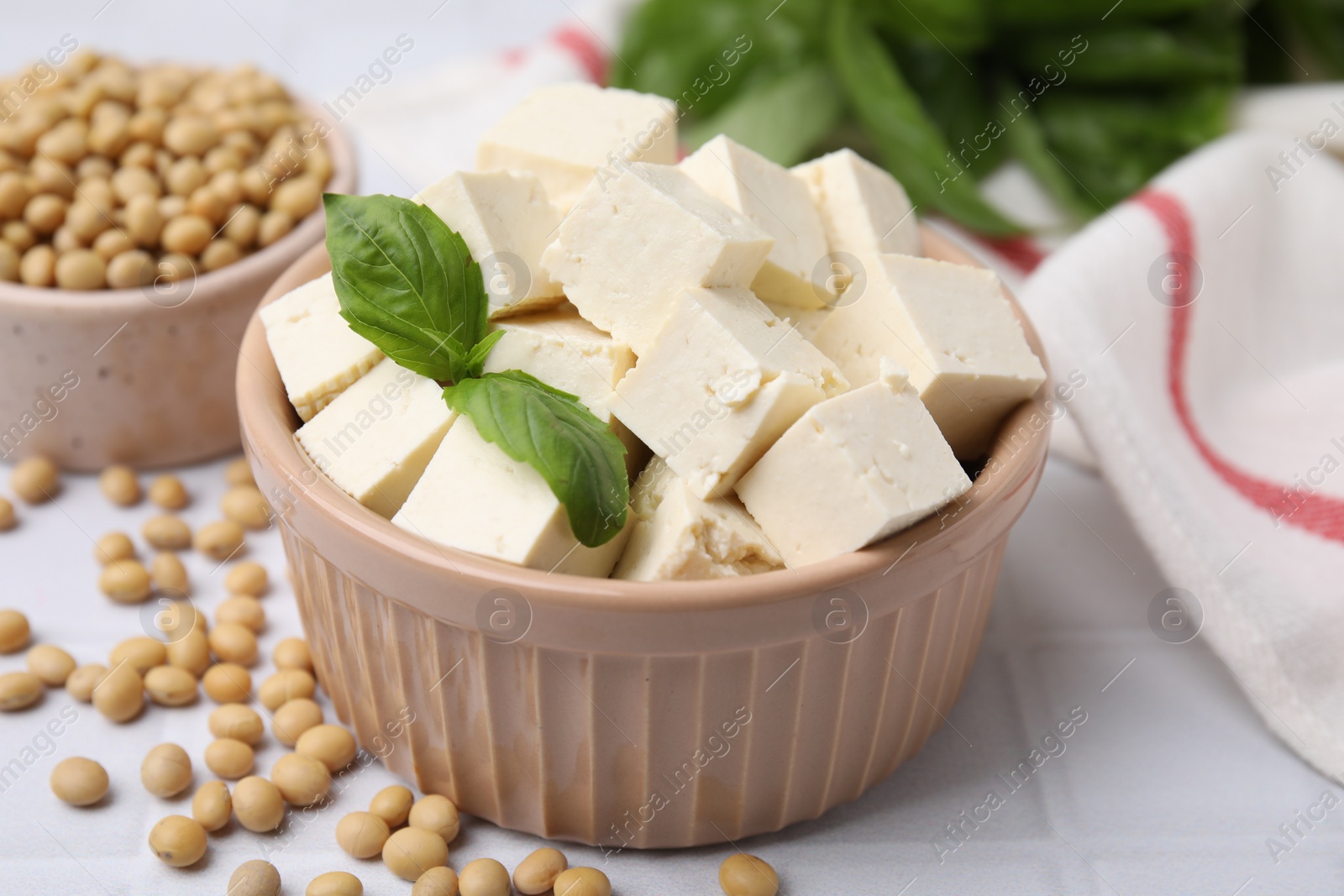 Photo of Delicious tofu cheese, basil and soybeans on white tiled table, closeup