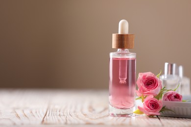 Photo of Bottle of essential rose oil and flowers on white wooden table against beige background, space for text