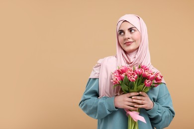 Photo of Happy woman in hijab with beautiful bouquet on beige background. Space for text