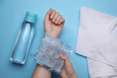 Woman with ice pack, bottle of water and towel on light blue background, top view. Heat stroke treatment