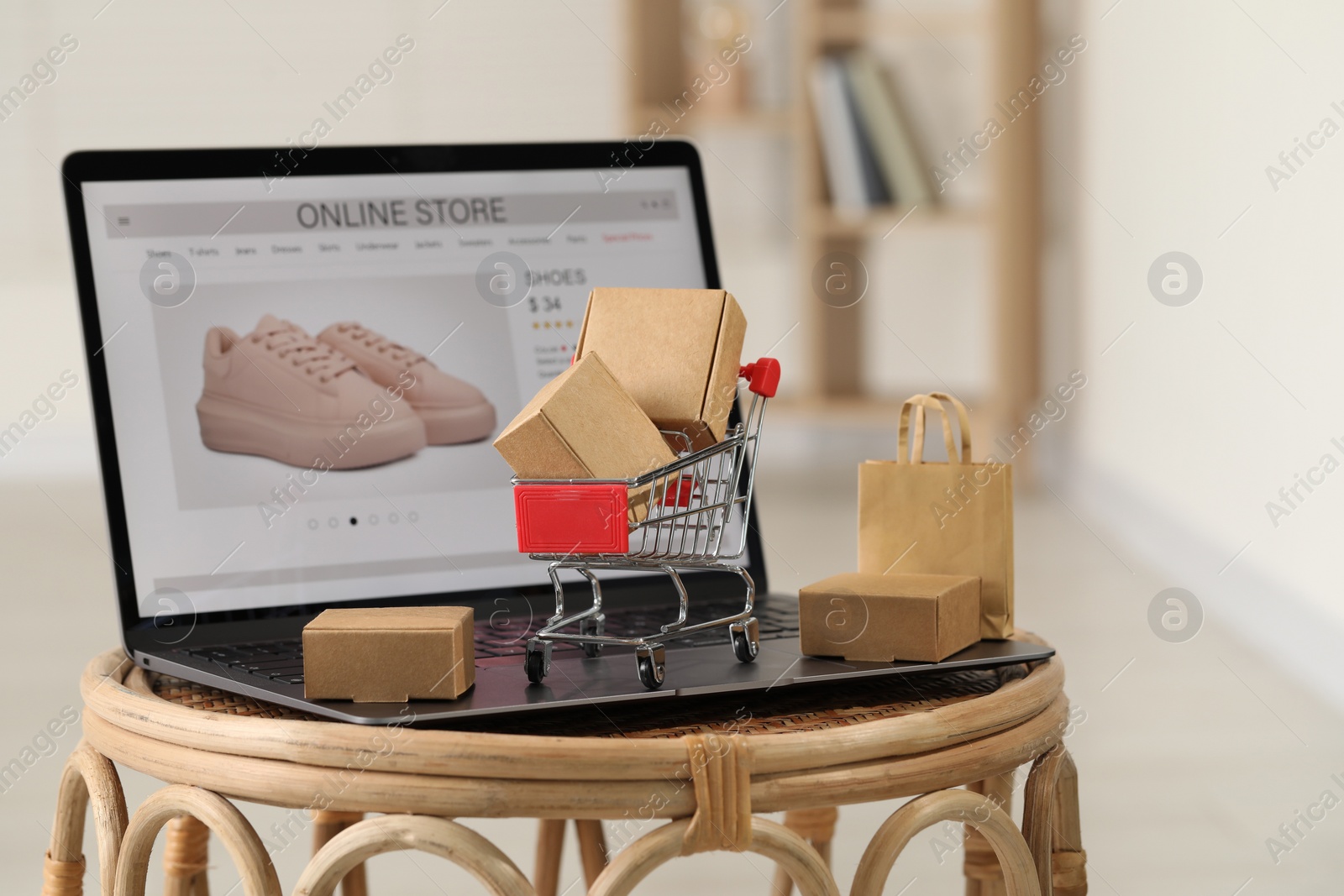 Photo of Online store. Laptop, mini shopping cart and purchases on table