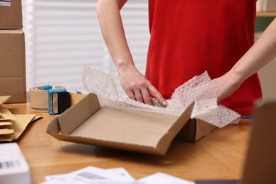 Photo of Post office worker packing parcel at wooden table indoors, closeup