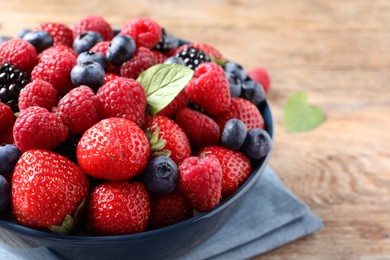 Different fresh ripe berries in bowl on wooden table, closeup