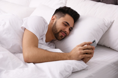 Young man addicted to smartphone in bed at home