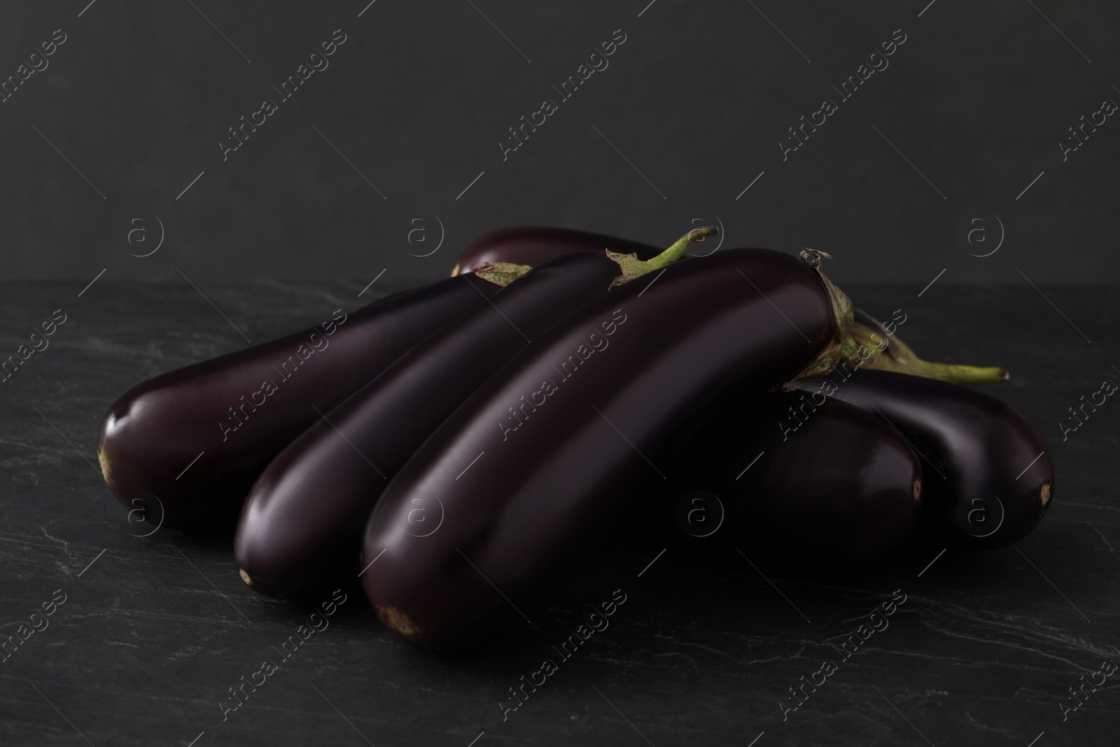 Photo of Pile of raw ripe eggplants on black table