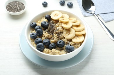 Tasty oatmeal with banana, blueberries and chia seeds served in bowl on white wooden table