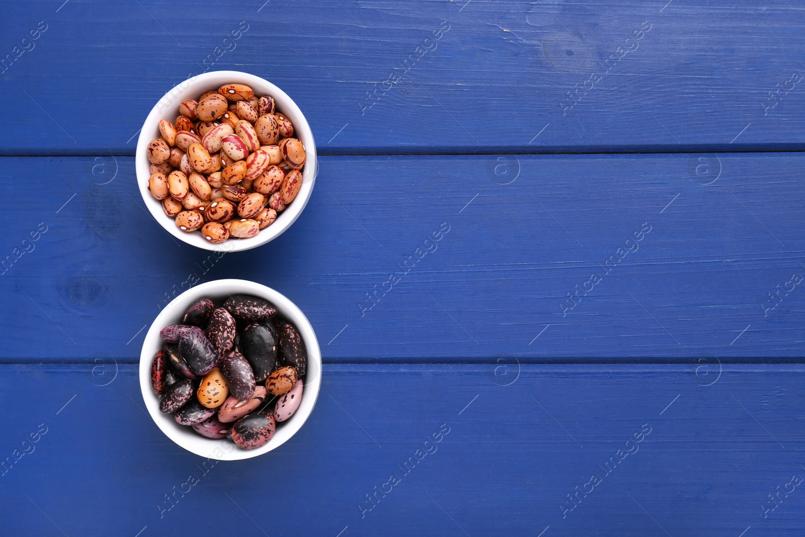 Photo of Different kinds of dry kidney beans on blue wooden table, top view. Space for text