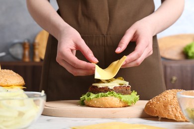 Woman making delicious vegetarian burger at white marble table, closeup