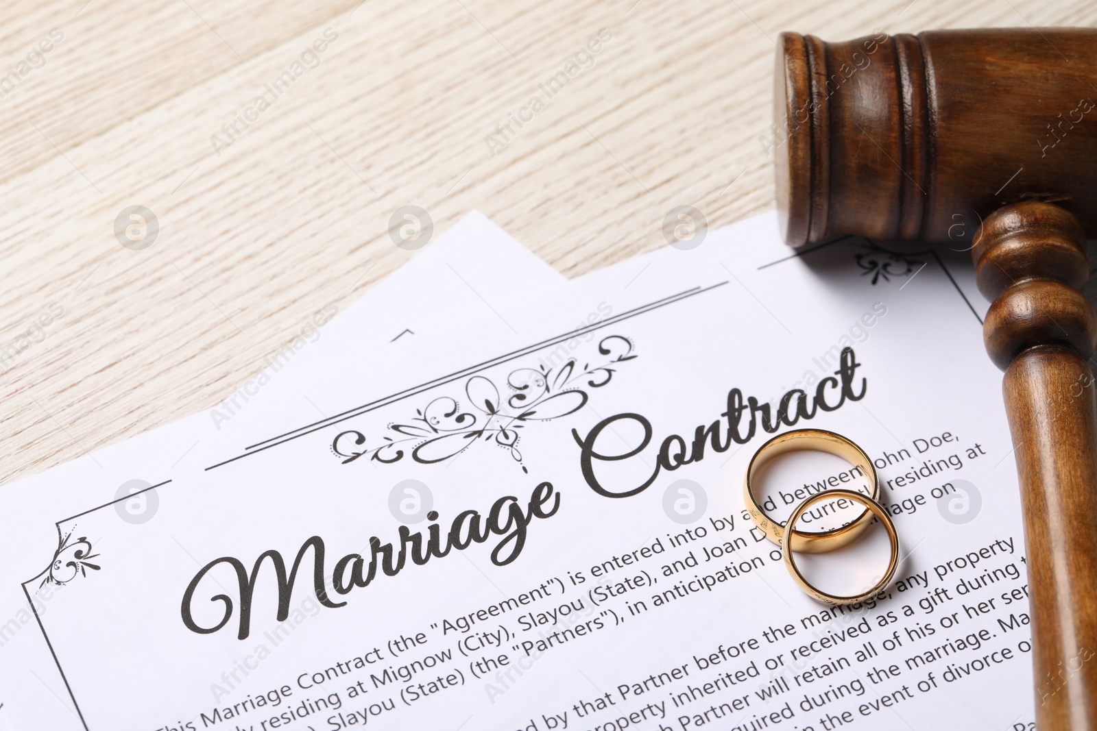 Photo of Marriage contract, golden wedding rings and gavel on wooden table, closeup