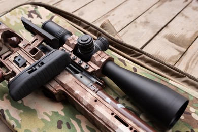 Closeup view of modern powerful sniper rifle with telescopic sight on wooden background