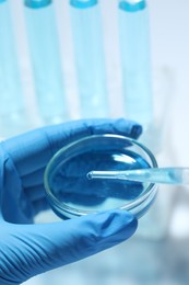 Scientist dripping liquid from pipette into petri dish on light background, closeup