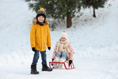 Little boy pulling sledge with his sister through snow in winter park