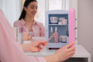 Photo of Woman taking face roller out of cosmetic refrigerator indoors, closeup