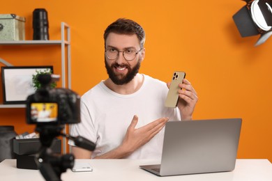 Smiling technology blogger with camera recording video review about smartphone at home