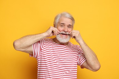 Senior man touching mustache on orange background