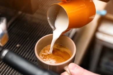 Photo of Male barista adding milk to coffee, closeup