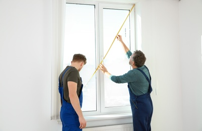 Service men measuring window for installation indoors