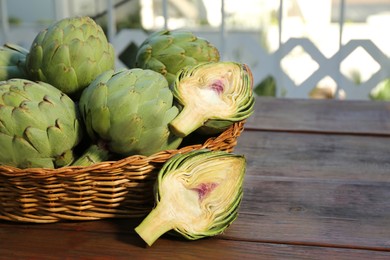 Photo of Wicker basket with fresh raw artichokes on wooden table. Space for text