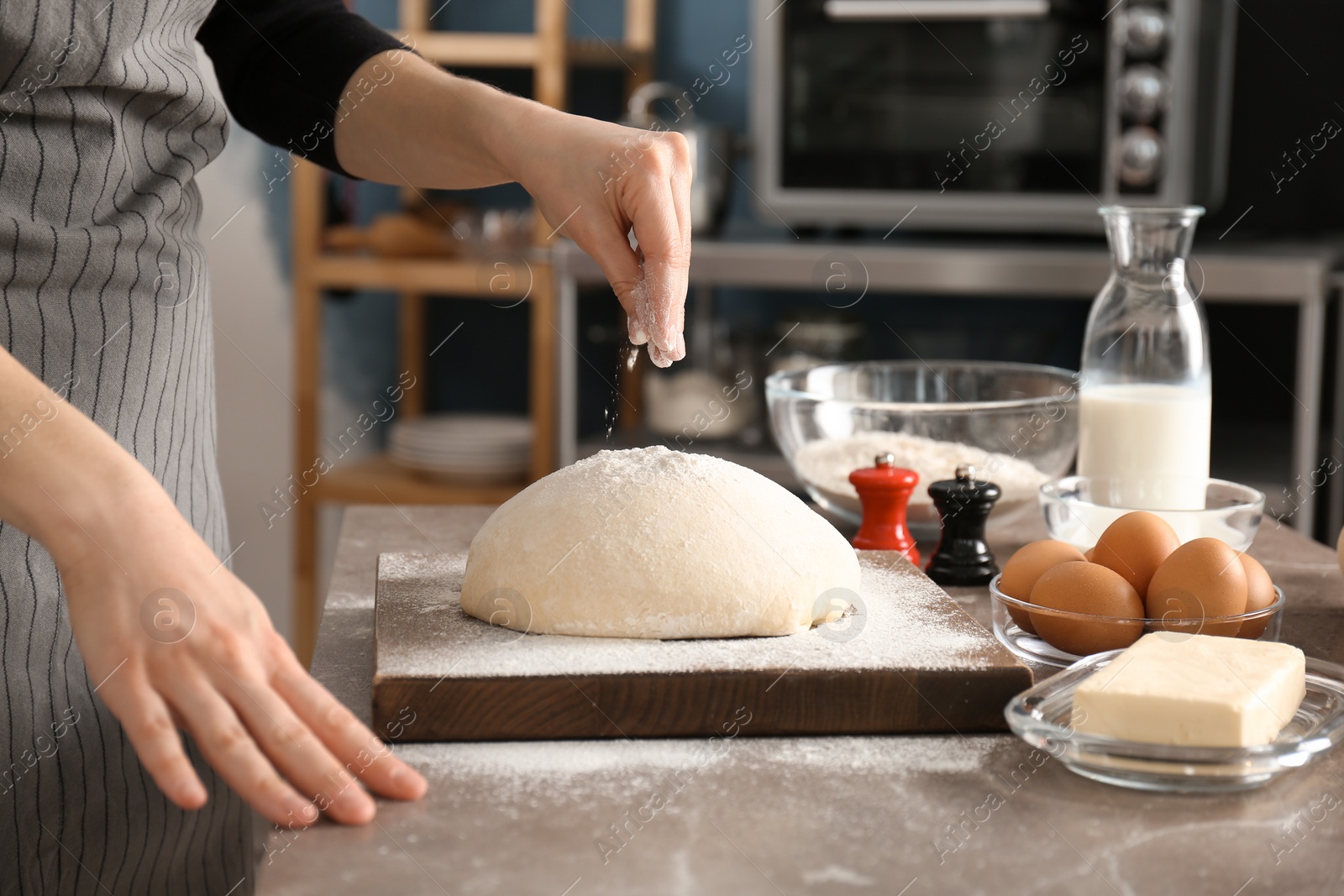 Photo of Woman sprinkling flour over dough on table in kitchen