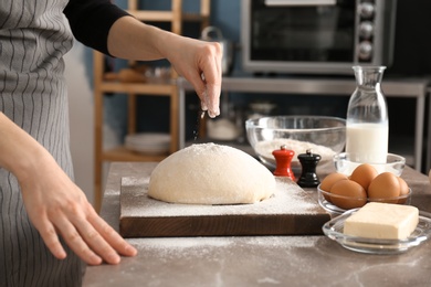 Woman sprinkling flour over dough on table in kitchen