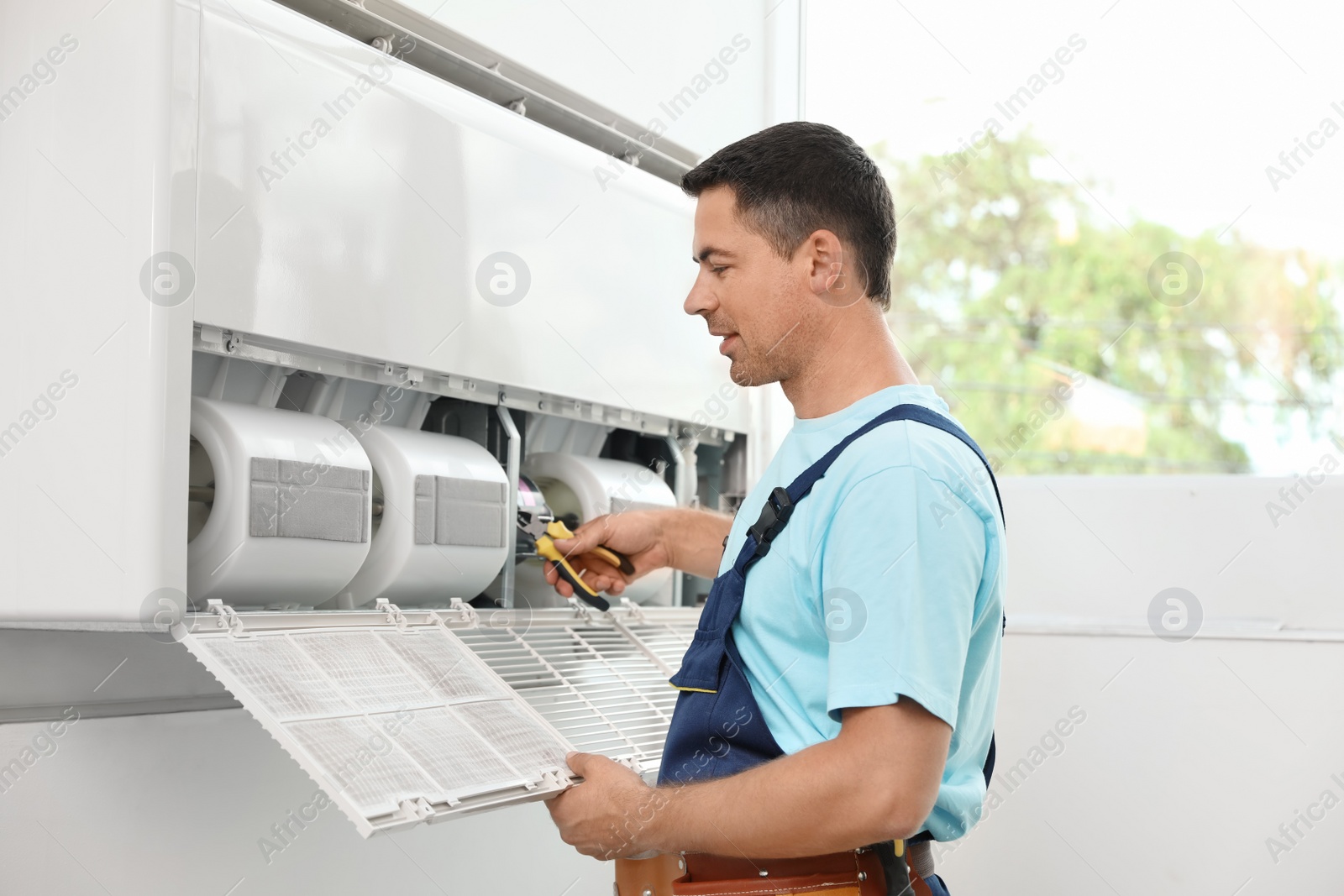 Photo of Male technician repairing modern air conditioner indoors