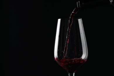 Photo of Pouring red wine into glass against black background, closeup. Space for text