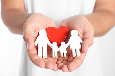 Photo of Young man holding wooden family figure and red heart on white background, closeup of hands