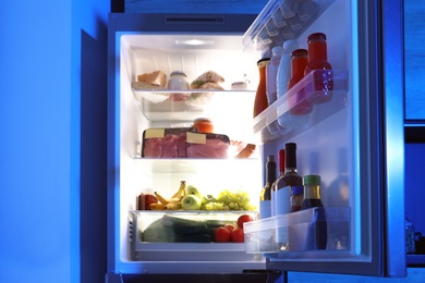 Photo of Open refrigerator full of products in kitchen at night