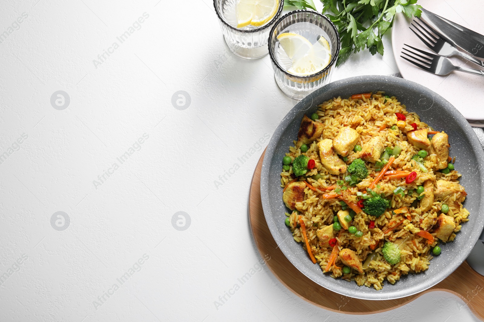 Photo of Tasty rice with meat and vegetables in frying pan served on white table, flat lay. Space for text