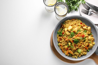 Photo of Tasty rice with meat and vegetables in frying pan served on white table, flat lay. Space for text