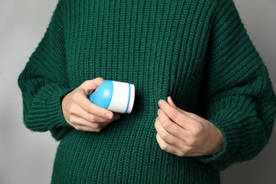 Woman in woolen sweater using fabric shaver on light grey background, closeup