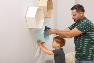 Father and son installing shelves on wall indoors. Repair work