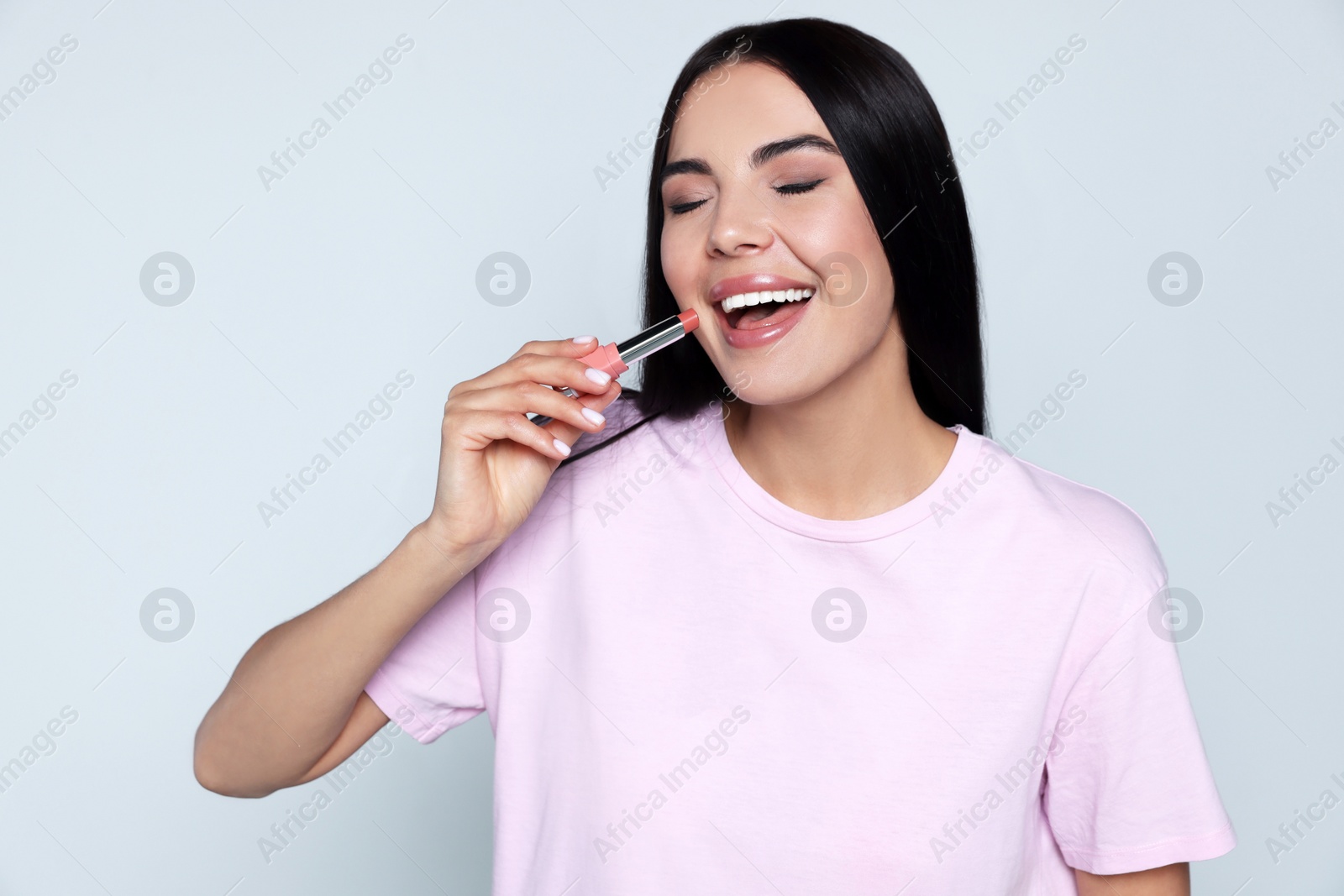 Photo of Young woman with beautiful makeup holding nude lipstick on light gray background