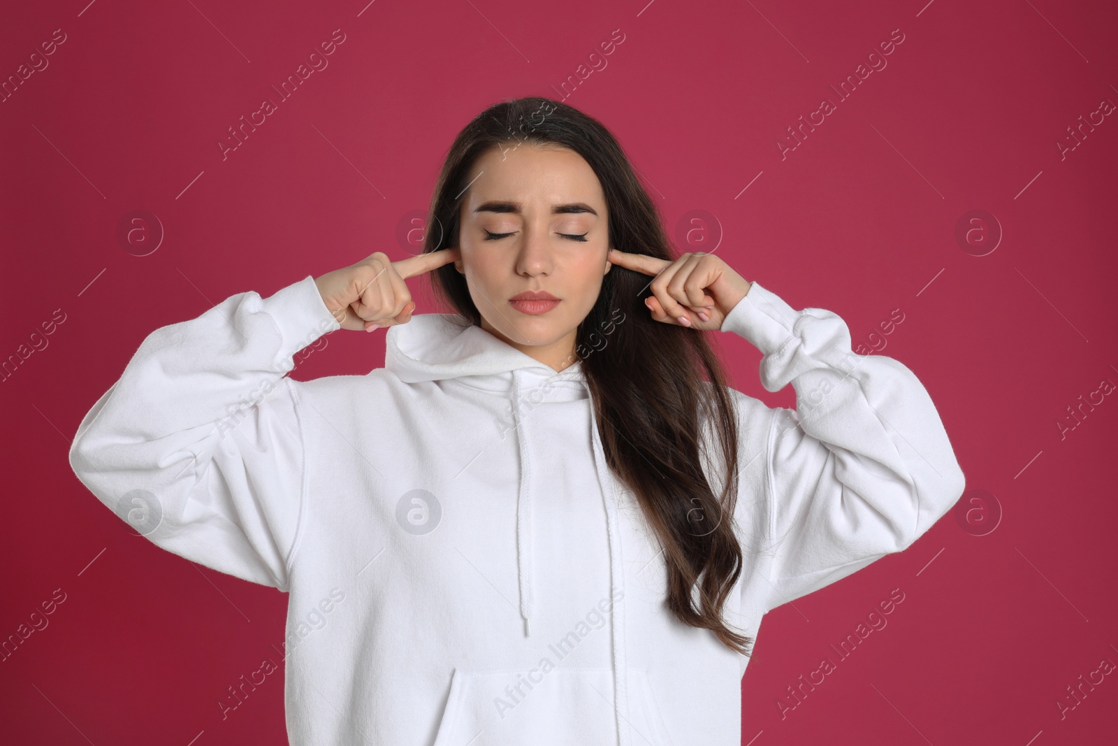 Photo of Young woman covering ears with fingers on pink background