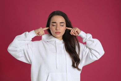 Young woman covering ears with fingers on pink background