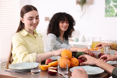 Photo of Vegetarian food. Friends eating fresh fruits at wooden table indoors