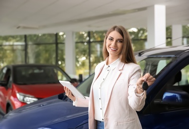 Photo of Woman with tablet and car keys in modern auto dealership