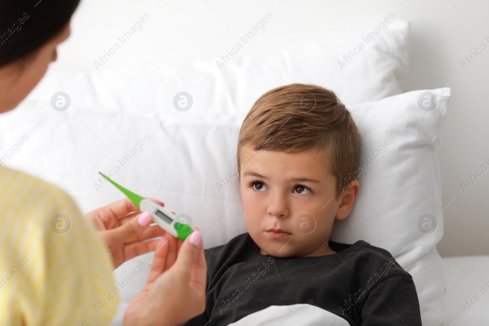 Photo of Mother measuring temperature of her sick son in bed