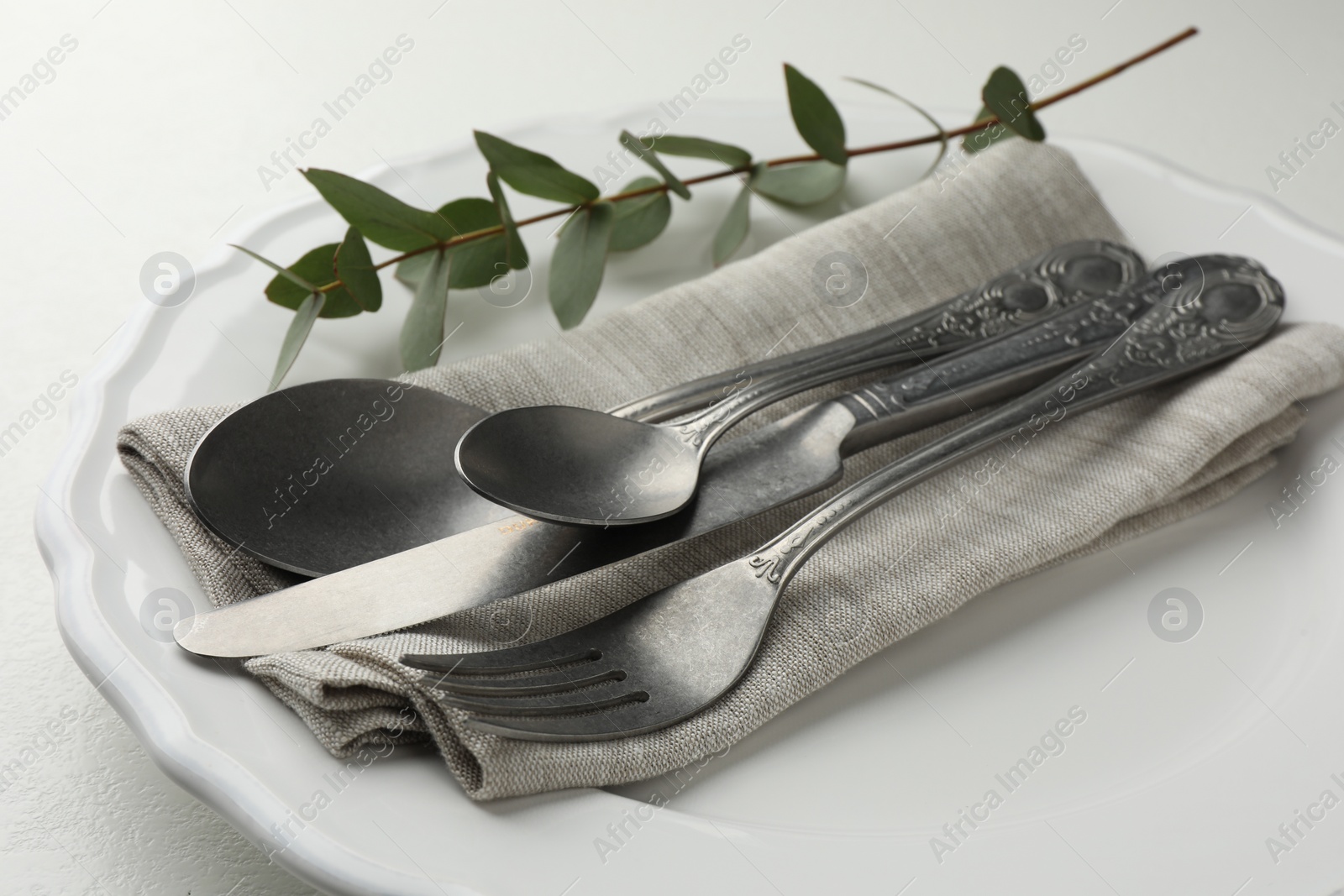 Photo of Stylish setting with cutlery, eucalyptus leaves and plate on white textured table, closeup