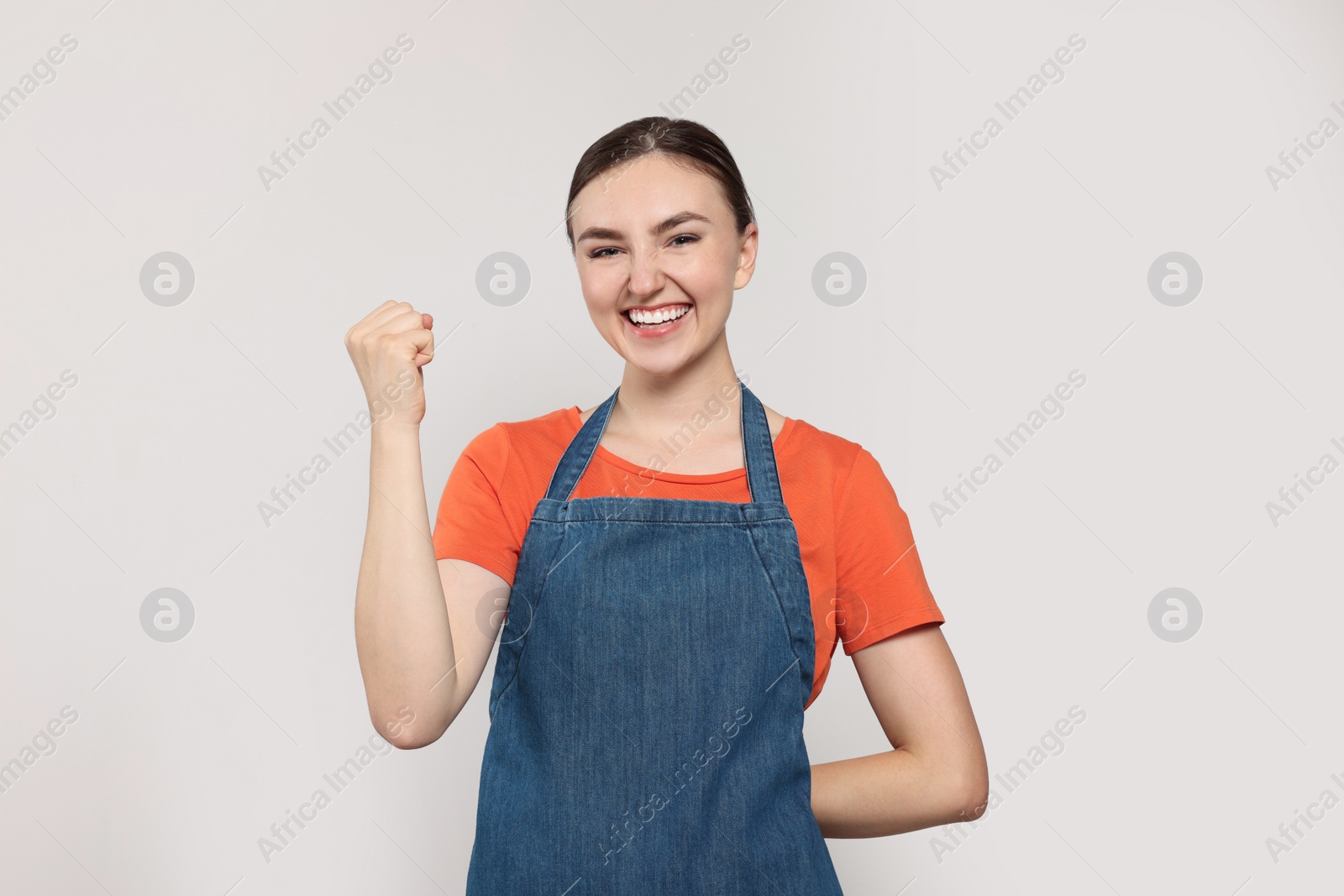 Photo of Beautiful young woman in clean denim apron on light grey background