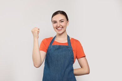 Photo of Beautiful young woman in clean denim apron on light grey background