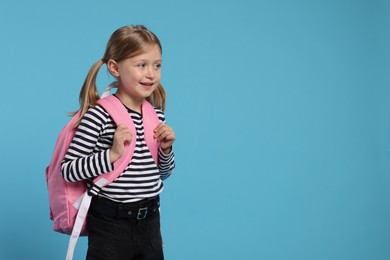 Photo of Happy schoolgirl with backpack on light blue background, space for text