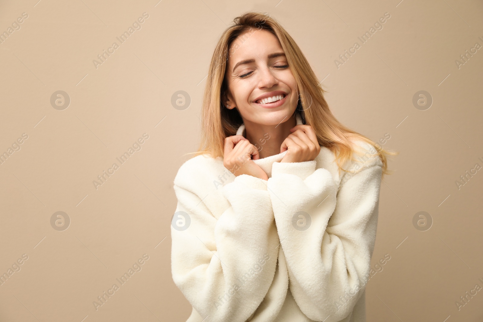 Photo of Beautiful young woman wearing knitted sweater on beige background