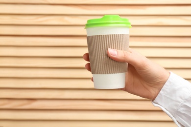 Woman holding takeaway paper coffee cup on wooden background. Space for text