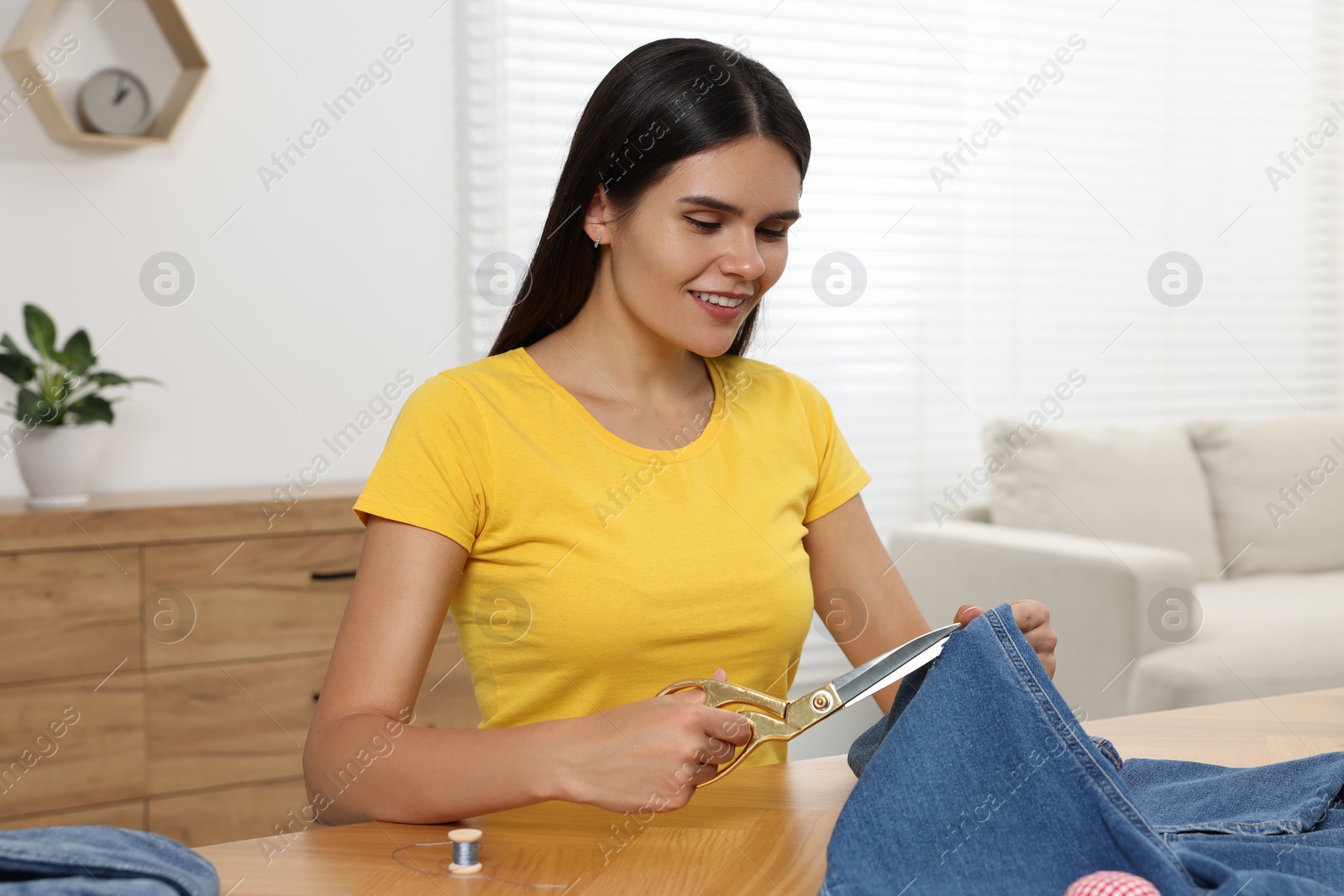 Photo of Young woman cutting jeans with scissors at wooden table indoors