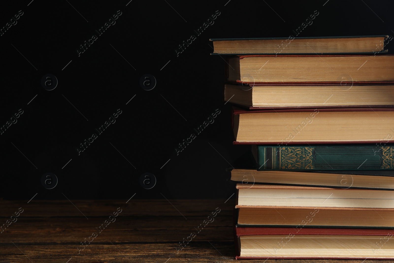 Photo of Collection of different books on wooden table against dark background. Space for text