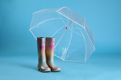 Photo of Open transparent umbrella and rubber boots on light blue background