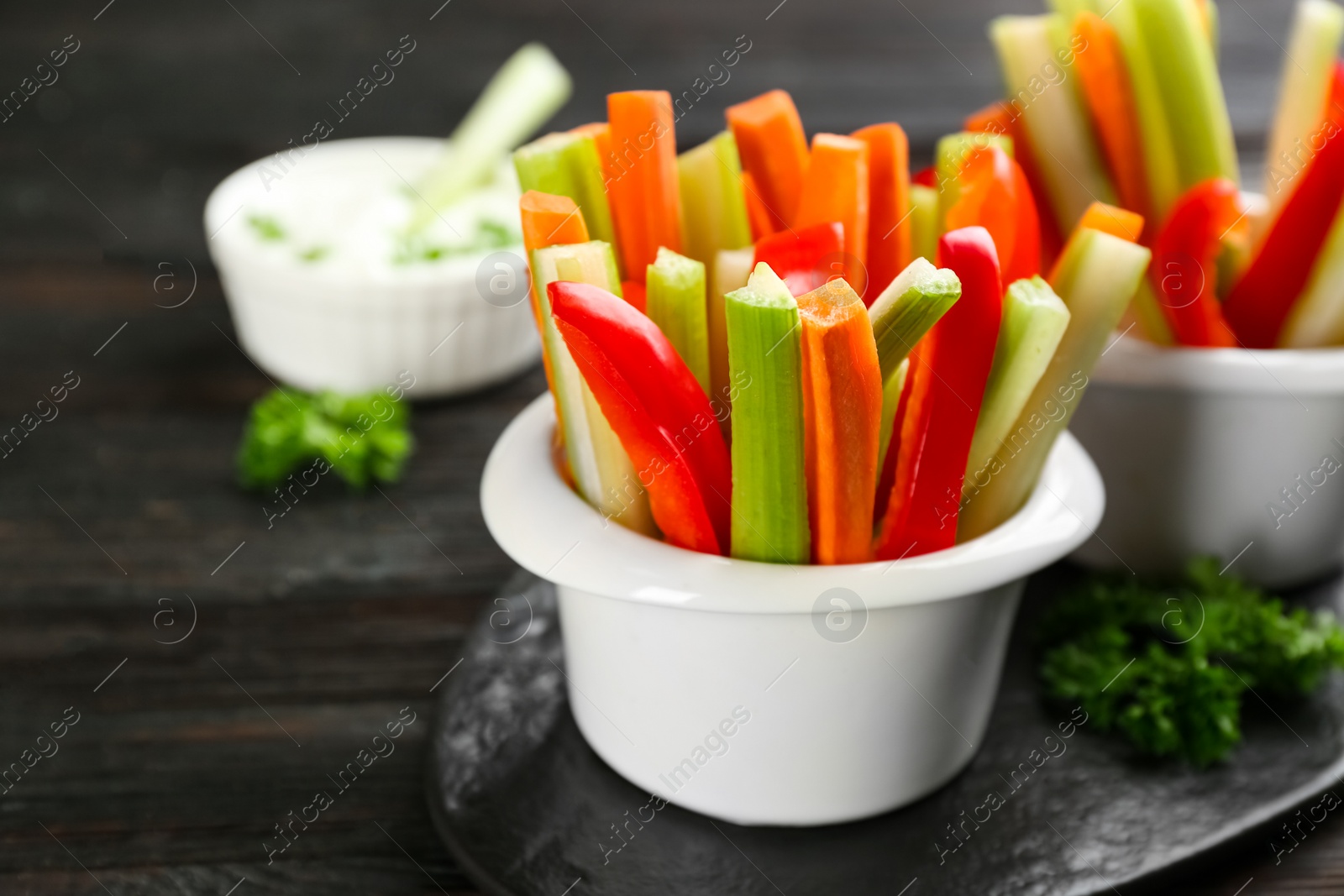 Photo of Celery and other vegetable sticks in bowls on dark wooden table, closeup. Space for text