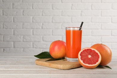 Photo of Tasty grapefruit juice in glass and fresh fruits on light wooden table against white brick wall. Space for text